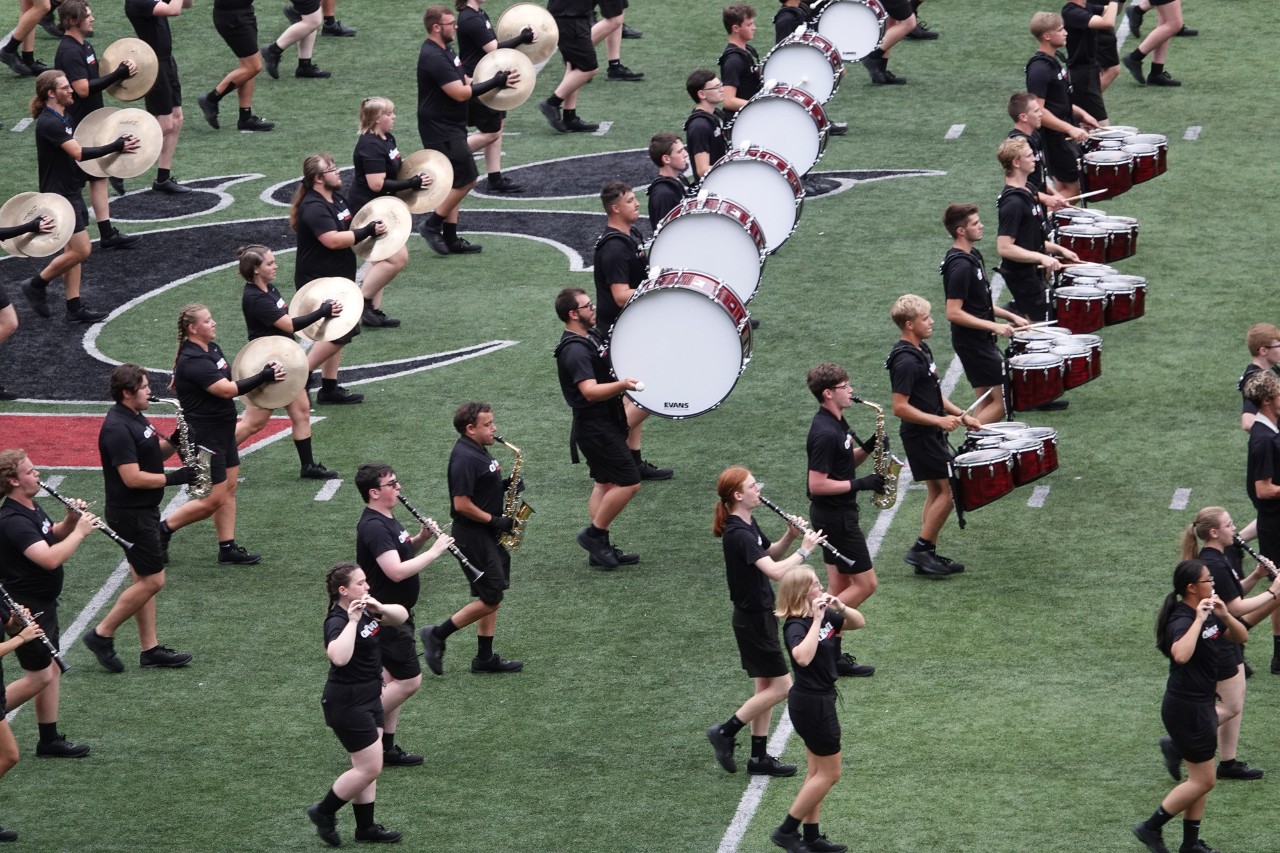 The UC Marching Band performs in matching black shorts and T-shirts.