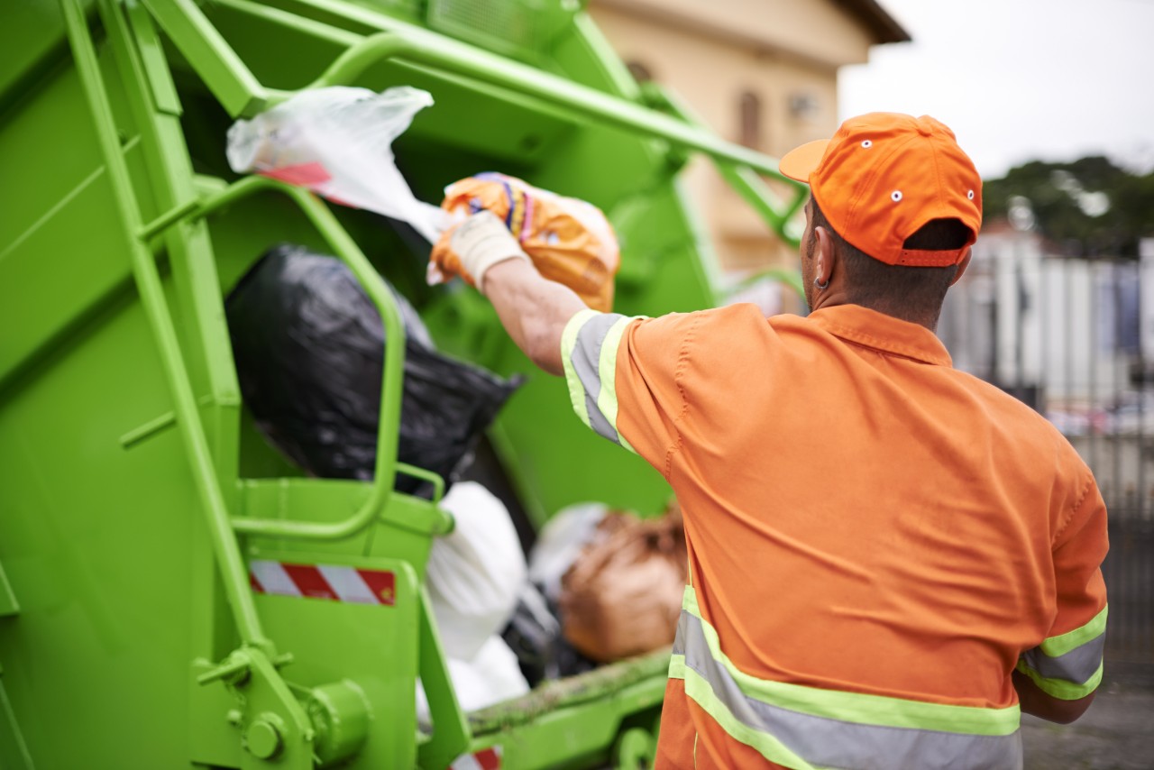 A garbage collector loads a garbage truck.