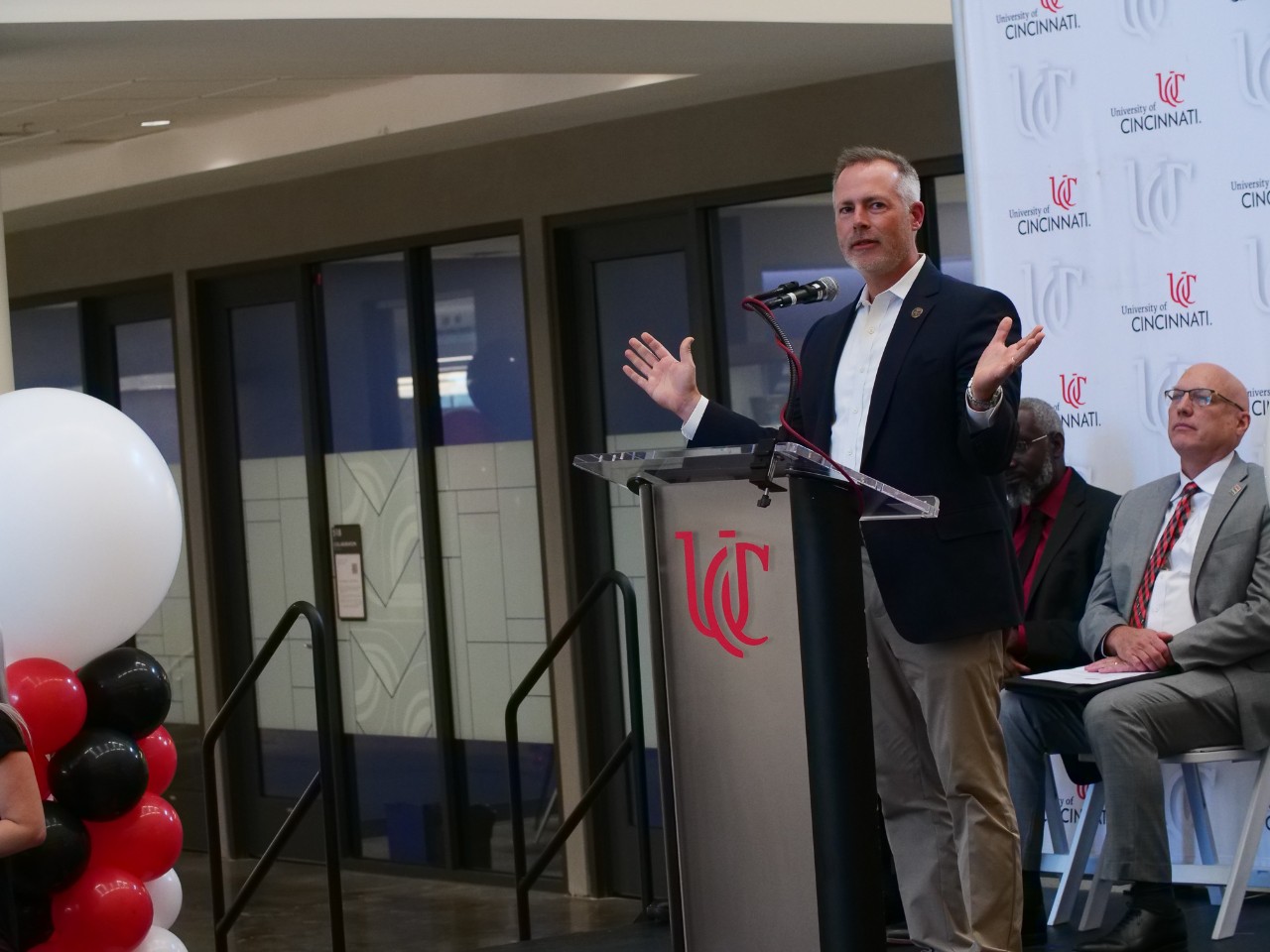 Robert Sprague stands at a podium in front of a branded UC background.