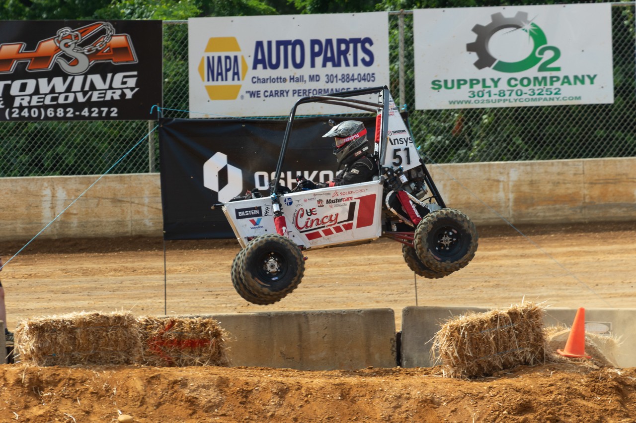 A Bearcats Baja car goes airborne over a dirt hill.