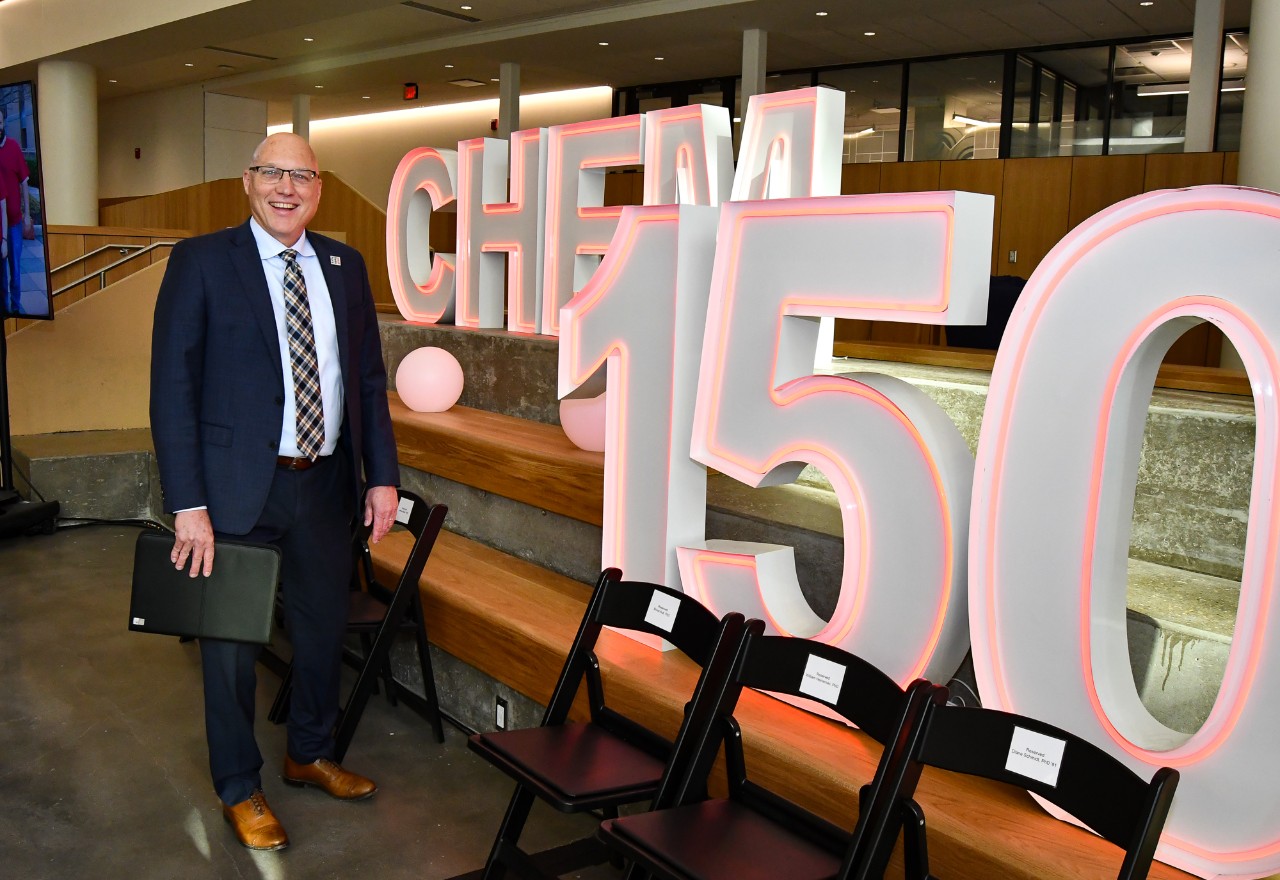 John Weidner stands in front of a neon sign reading Chem 150.