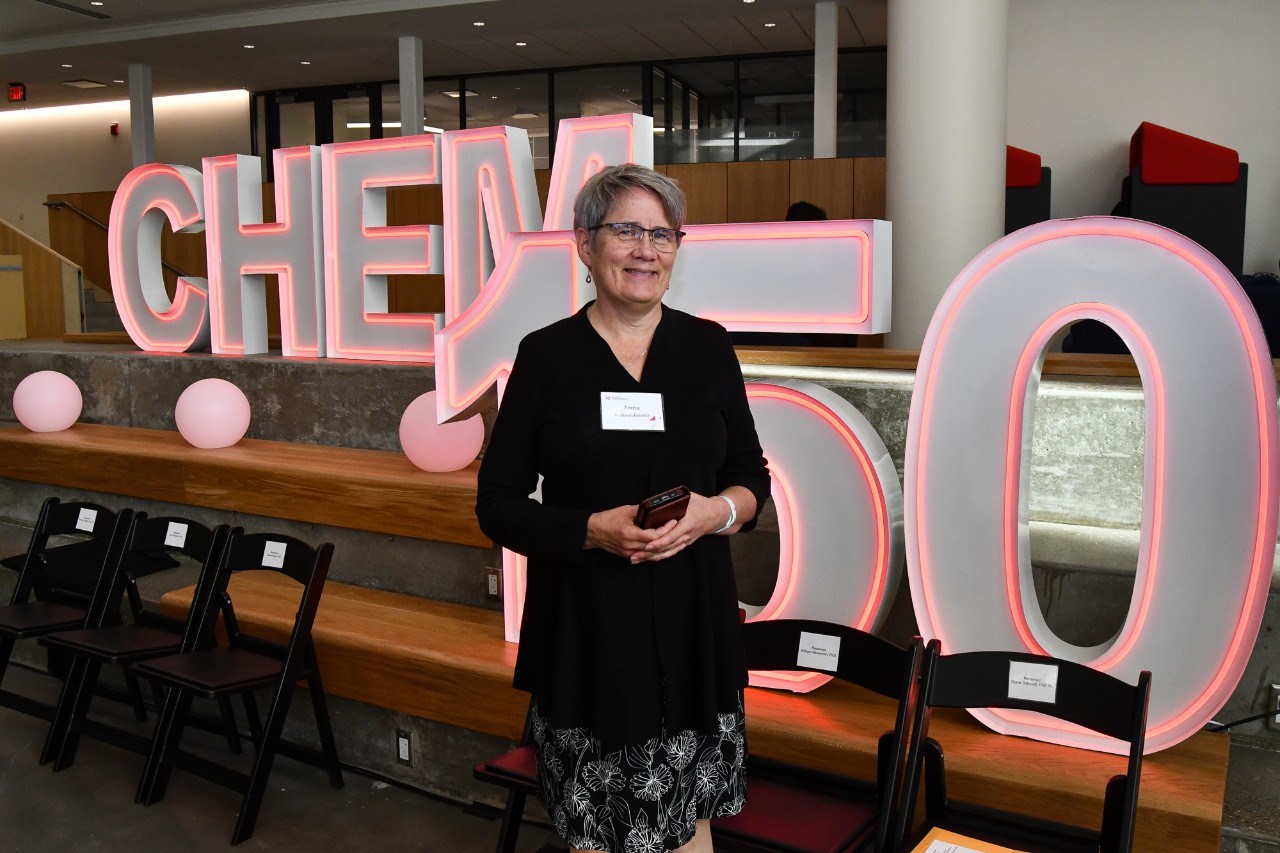 Anna Gudmundsdottir stands in front of a neon Chem 150 sign in the atrium of Old Chem.