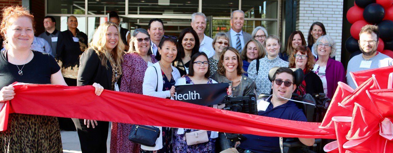Several people stand behind a large red ribbon