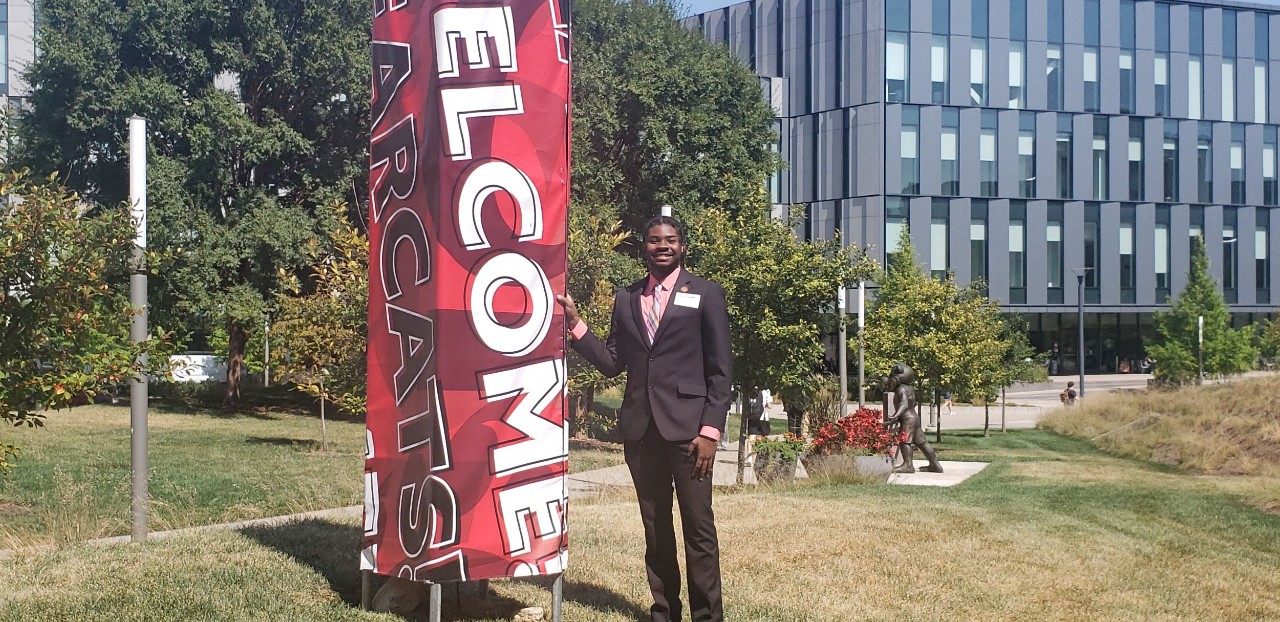 Photo Jalen Tucker standing on UC campus next to Welcome sign