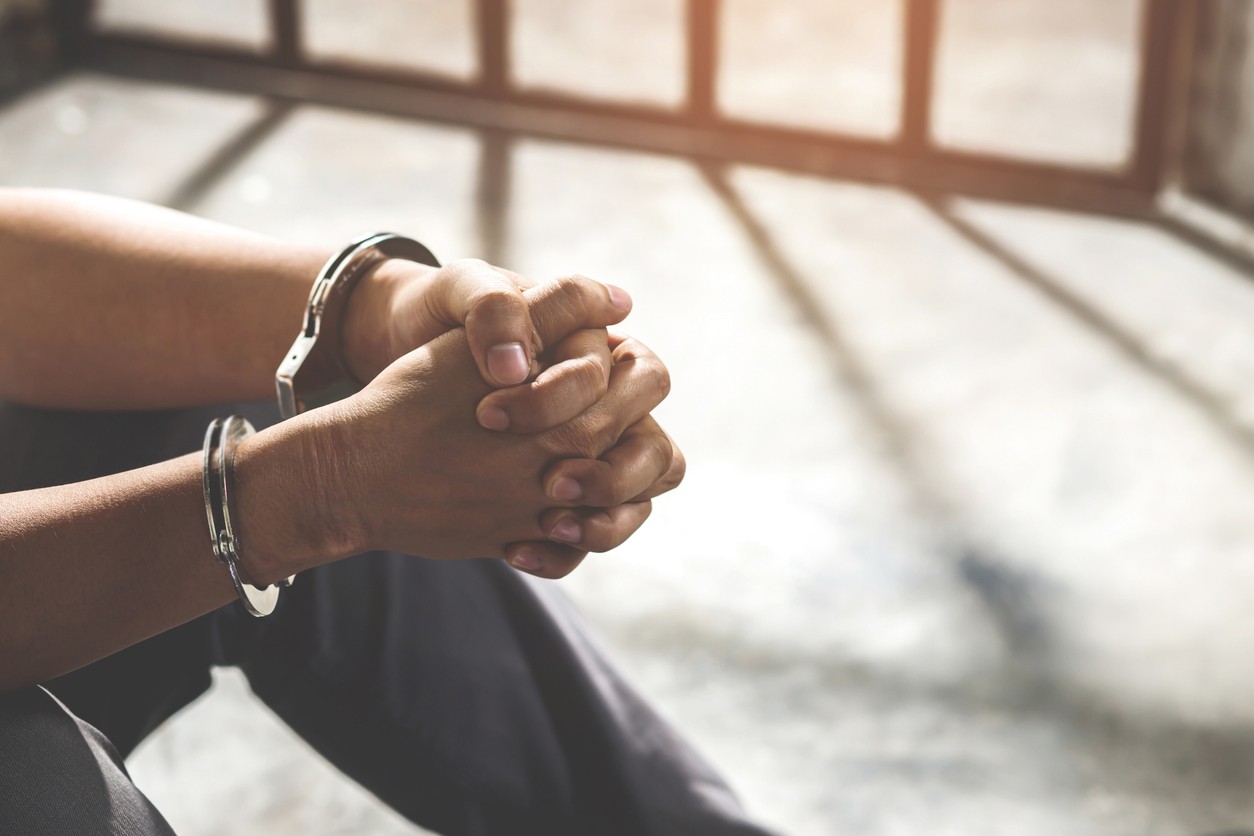 Person with handicuffs sitting behind bars