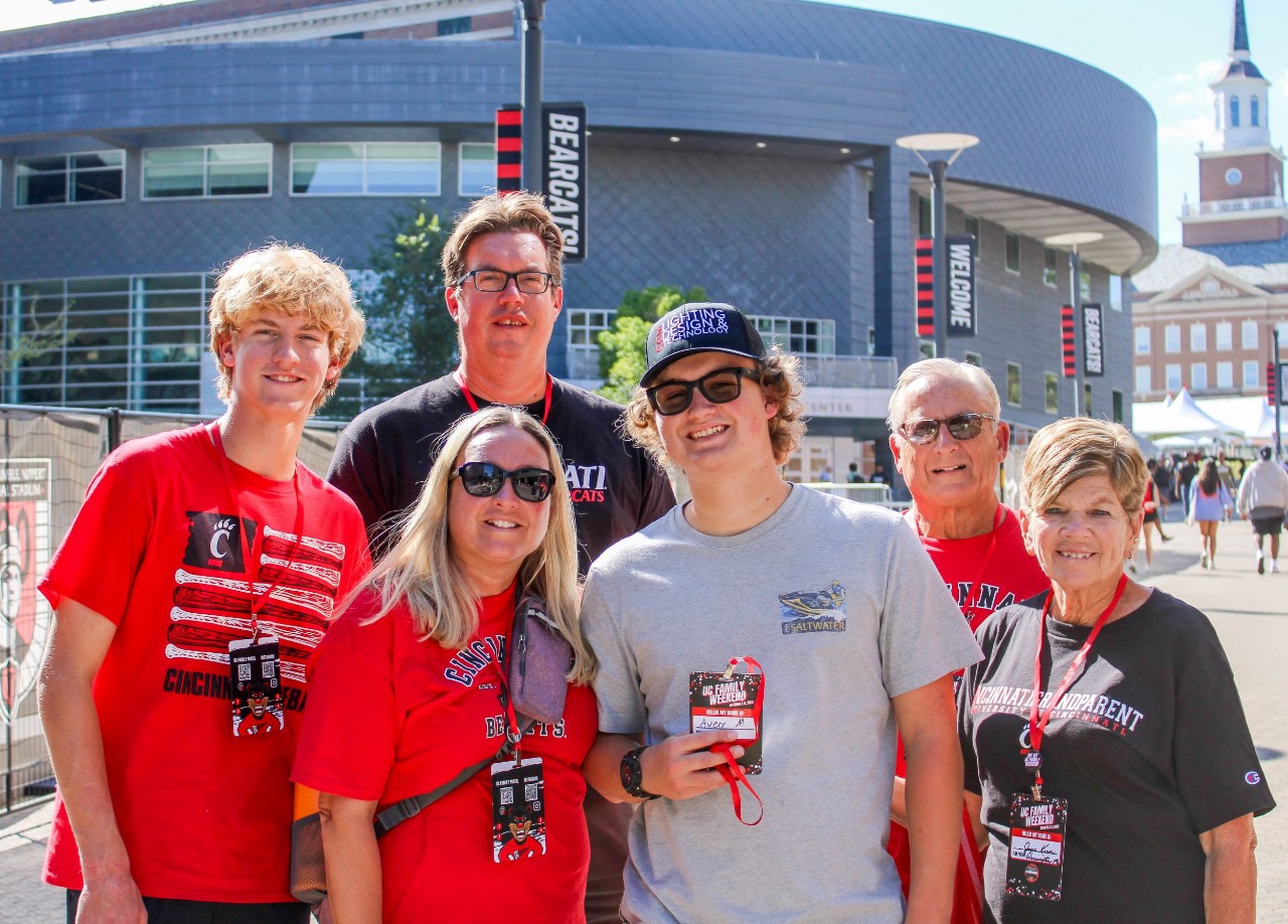 Family of six including Bearcat brothers, father, mother and grandparent wear UC swag and pose in front of TUC.