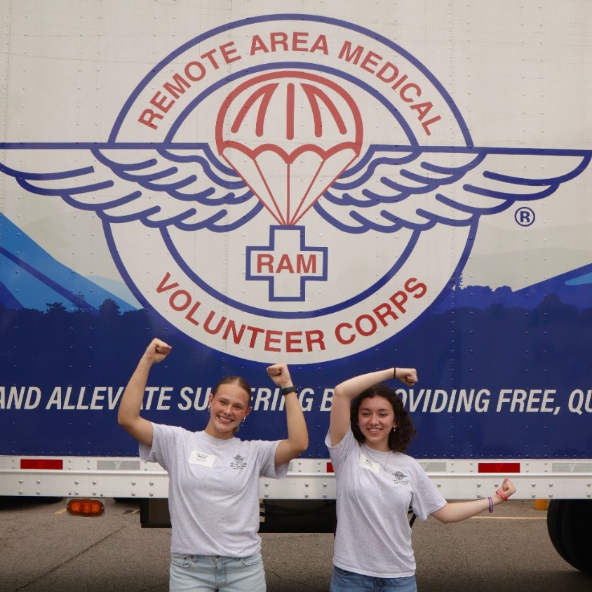 Davis (with a friend) stand in front of a Remote Area Medical truck with their arms up to spell "UC"