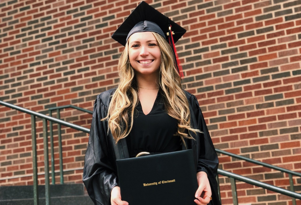 Sam Hillman, UC Bearcat for Life, stands at graduation holding her degree