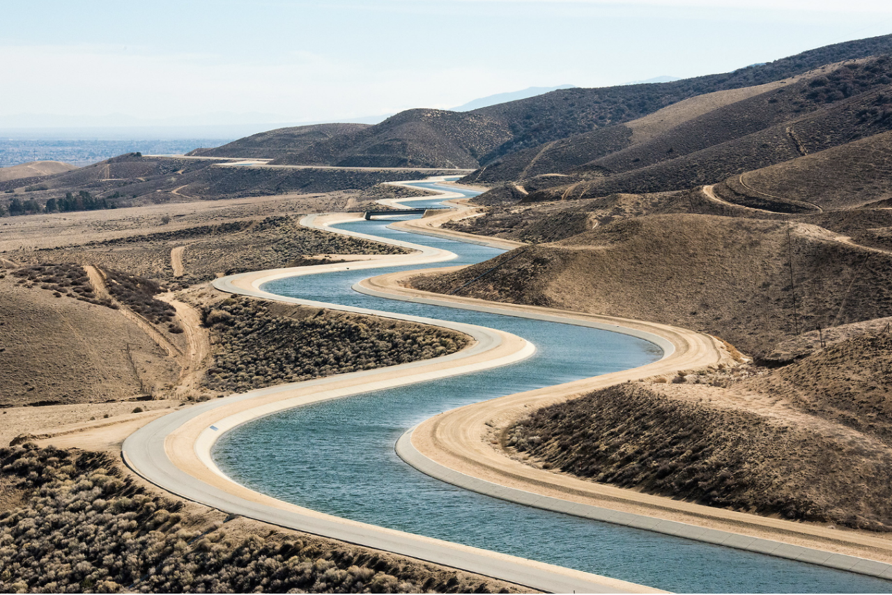 A blue water canal weaves back and forth across a hilly California landscape.