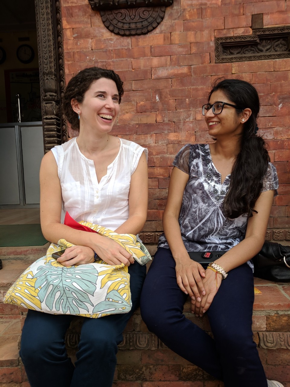 Two women sit on steps laughing in conversation.