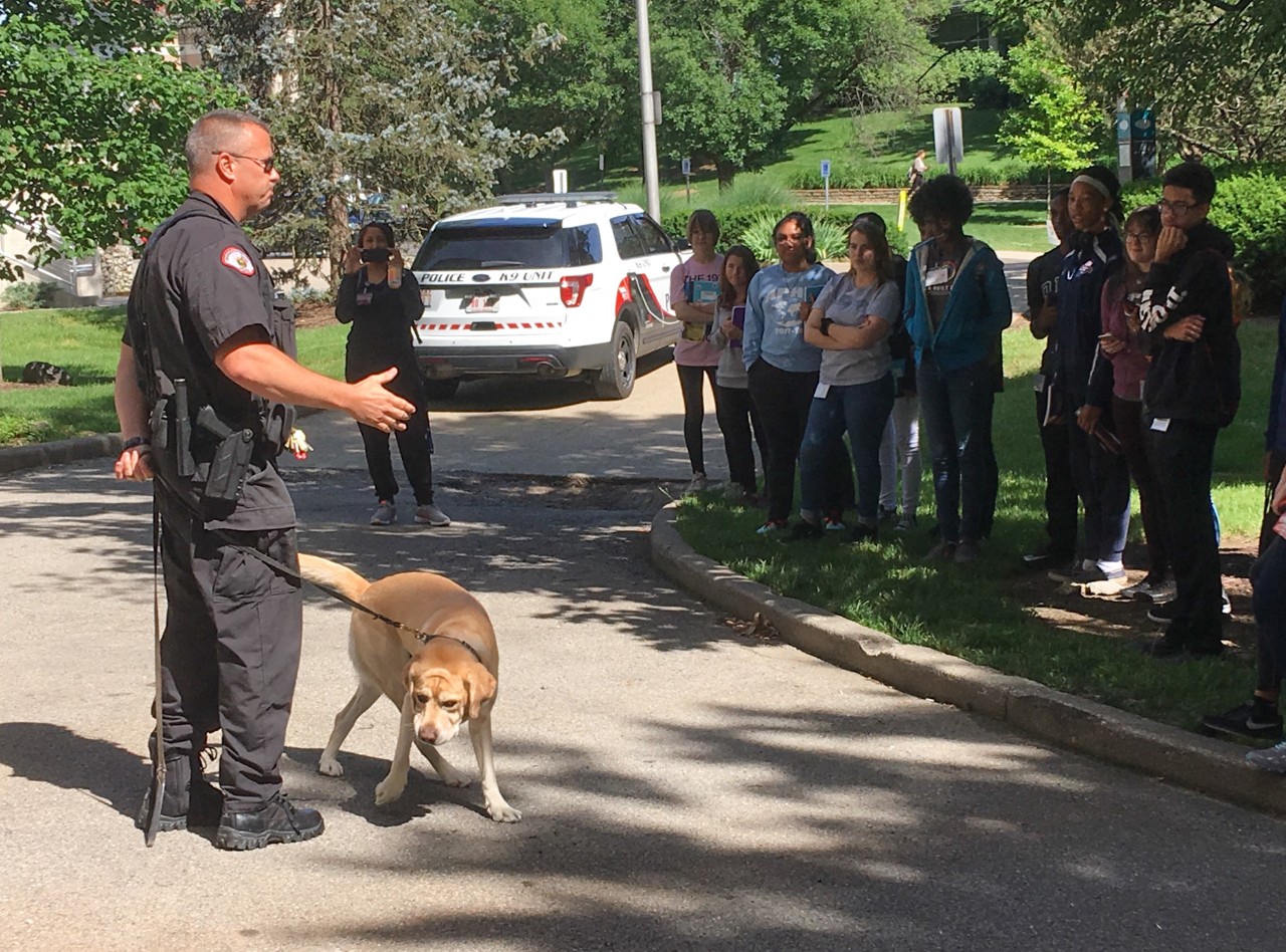 A police officer and his explosives-detection dog stand in front of a group of students during a demonstration on UC's campus.