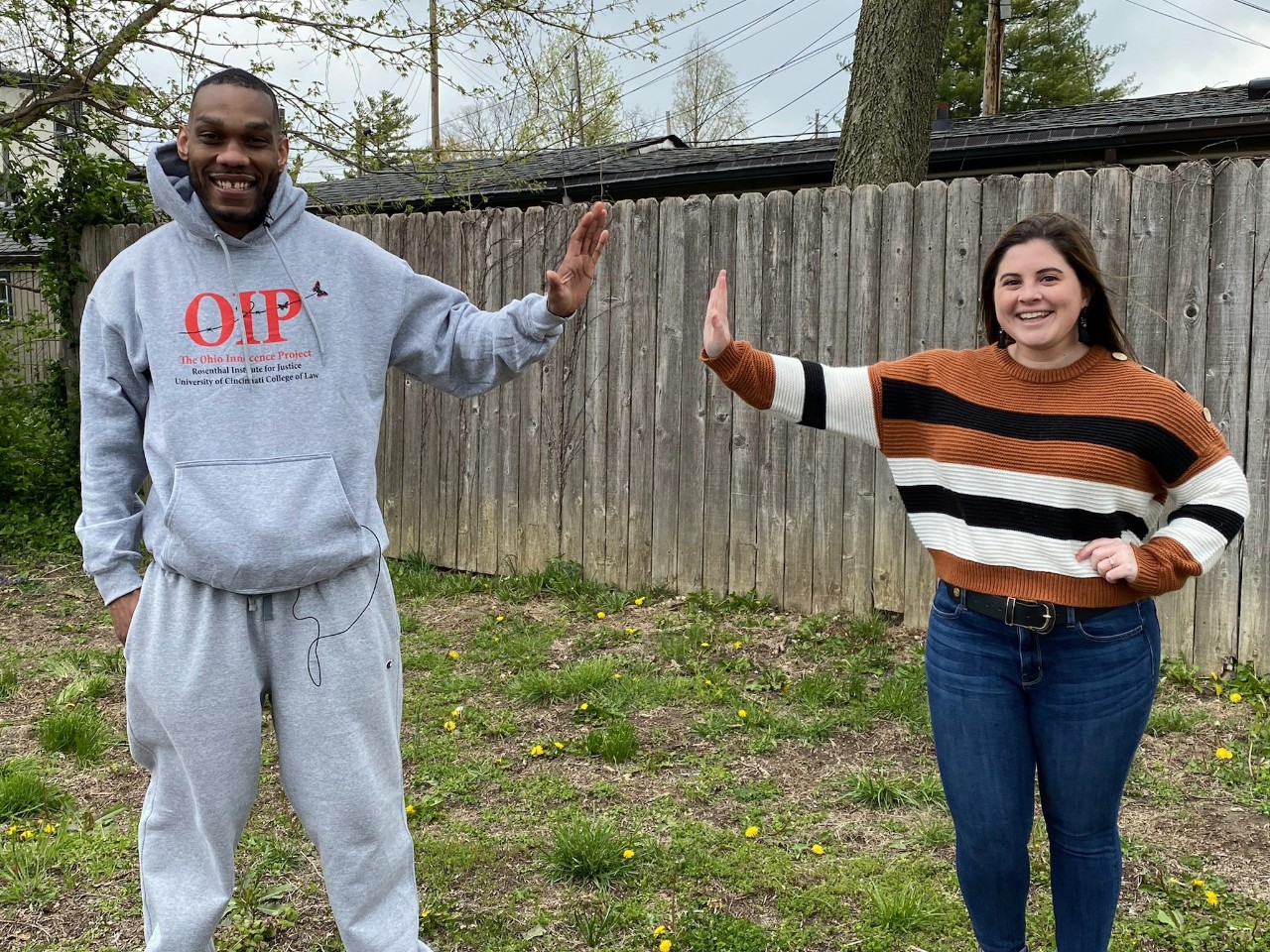 a man in a grey sweatshirt and jogging pants gives a high five from a distance to a woman wearing a striped sweater and jeans