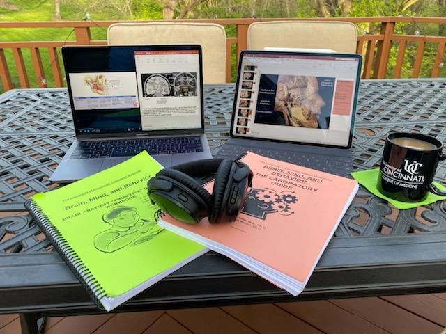 A table covered by a laptop, books, headphones and a drink
