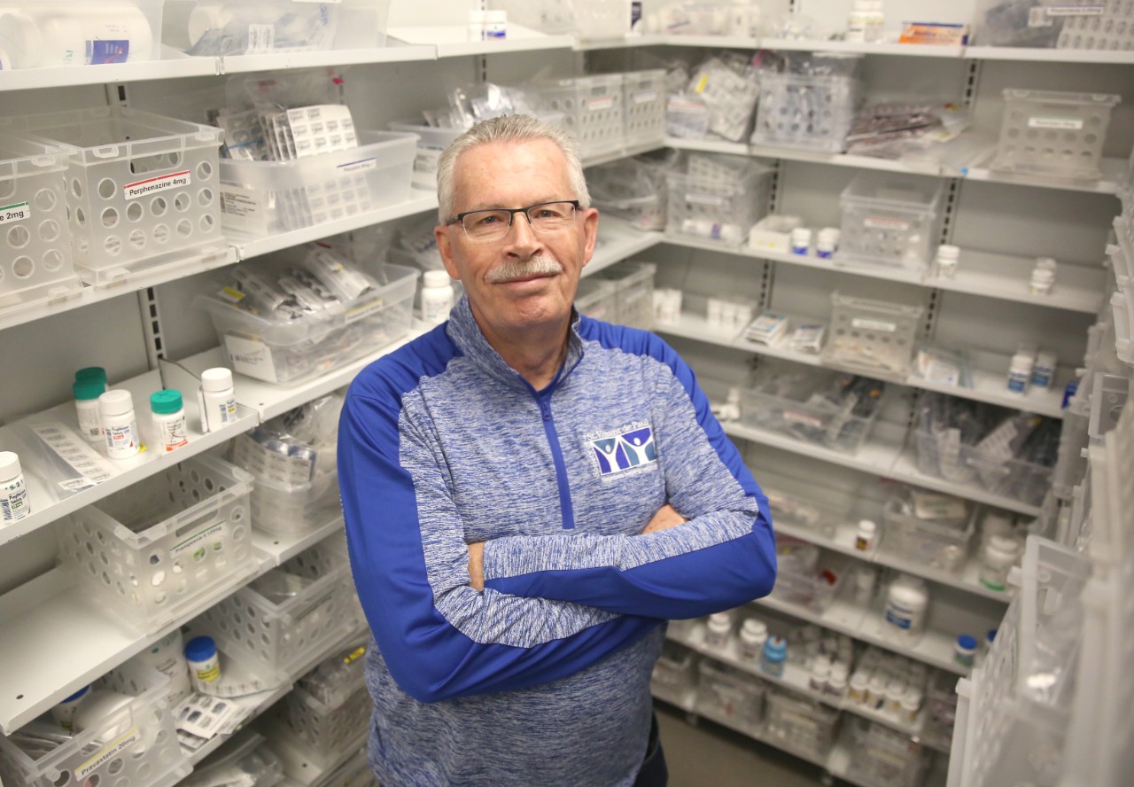 A man standing with his arms crossed in a room of pharmaceutical medicines