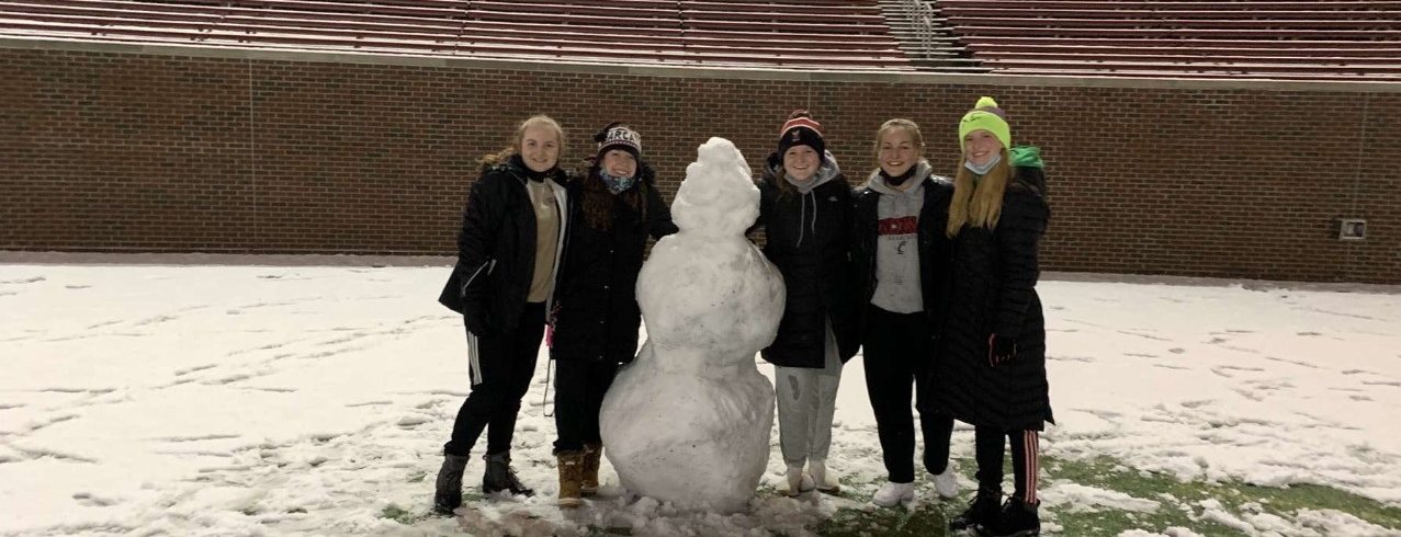 5 students on Nippert Stadium's field posing with a snowman they made