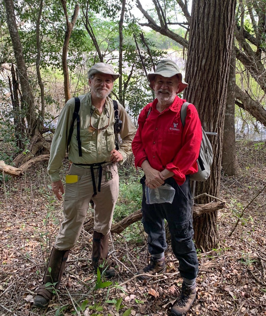 Two researchers wearing boots and backpacks pose for a photo in the rainforest.