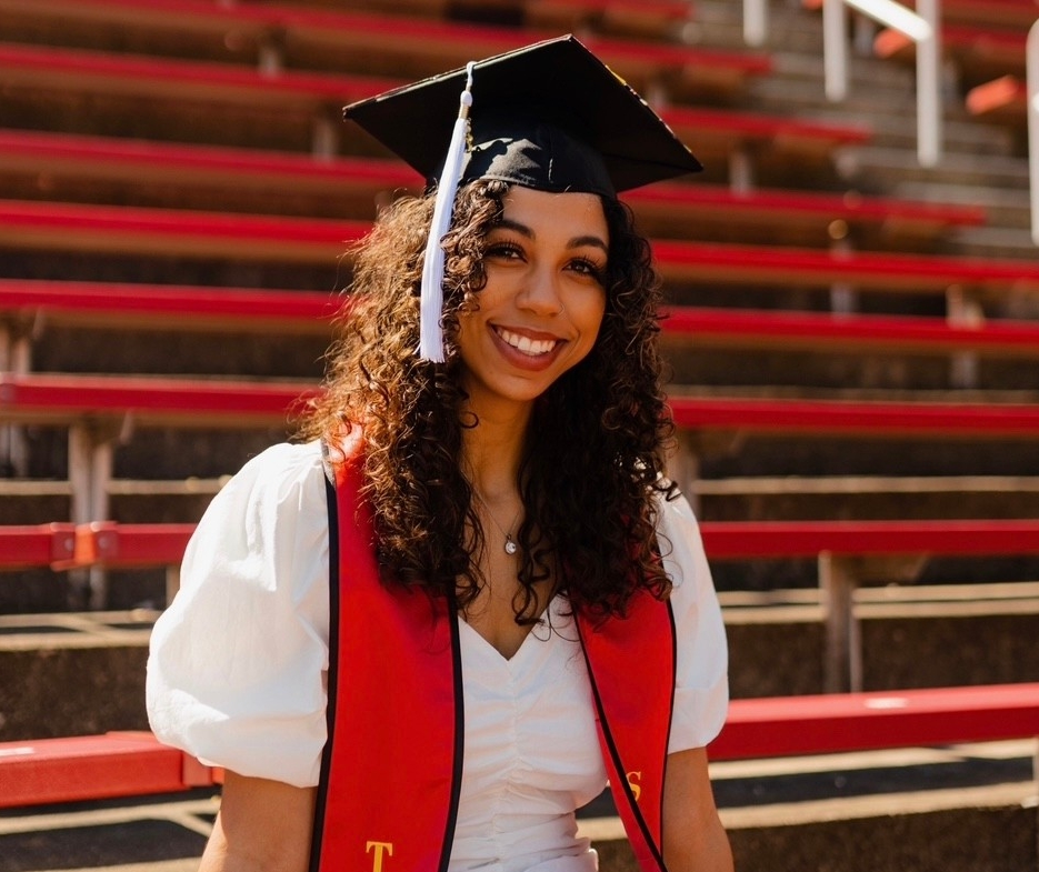 Taylor Allgood poses in her graduation cap in the bleachers at Nippert Stadium.