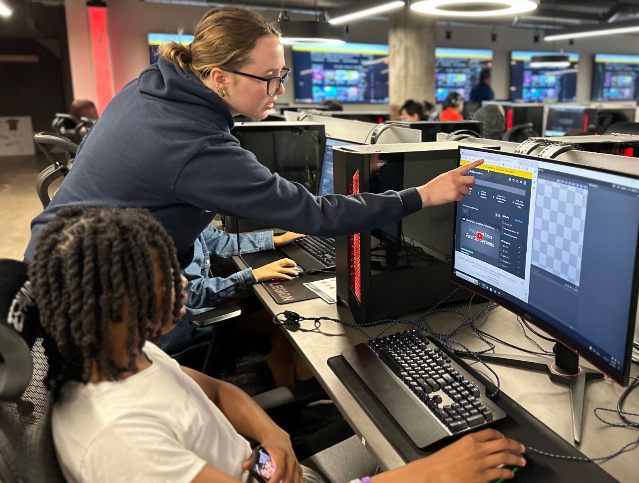 A teaching assistant helps a high school student on a computer.