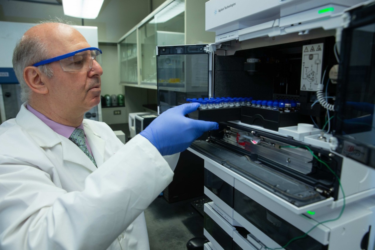 professor Dionysiou in a white coat holding a tray of small vials in a lab