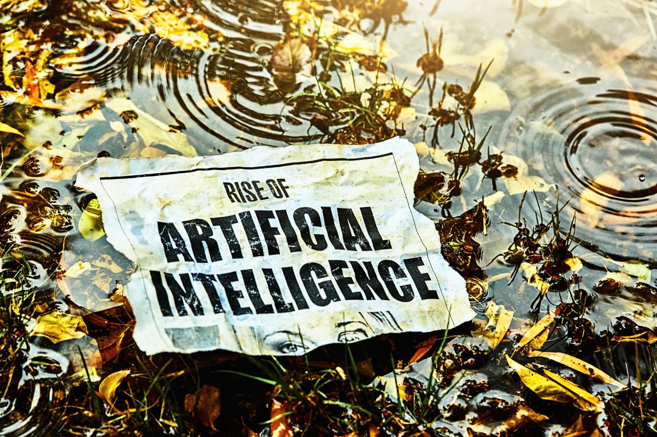 1467864574 Cut-out newspaper headline about the Rise of Artificial Intelligence, lying discarded in a marsh in the rain.
