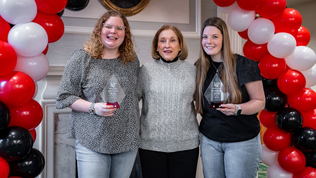 two students stand with faculty presenter under an arch made of balloons