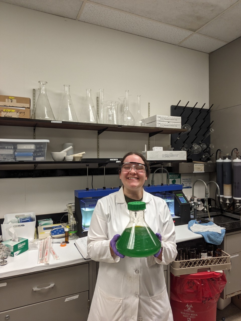 woman in a lab coat holds up a large beaker full of green liquid