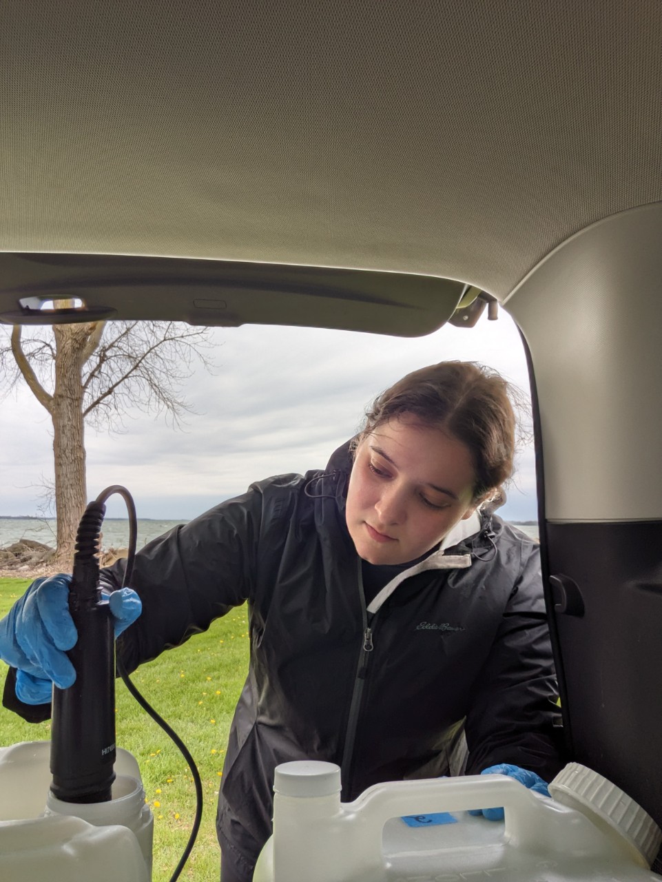 Woman leans over a small water tank and puts a testing tool inside it.