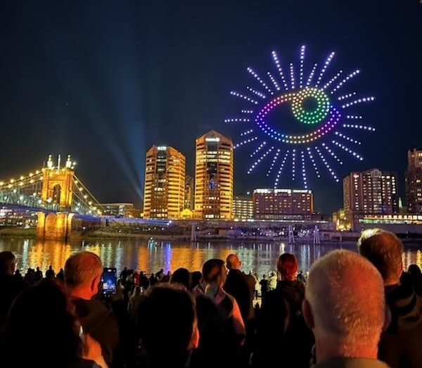 Hundreds of people stand on banks of Ohio River to watch drone show. Big eye blinking in the sky