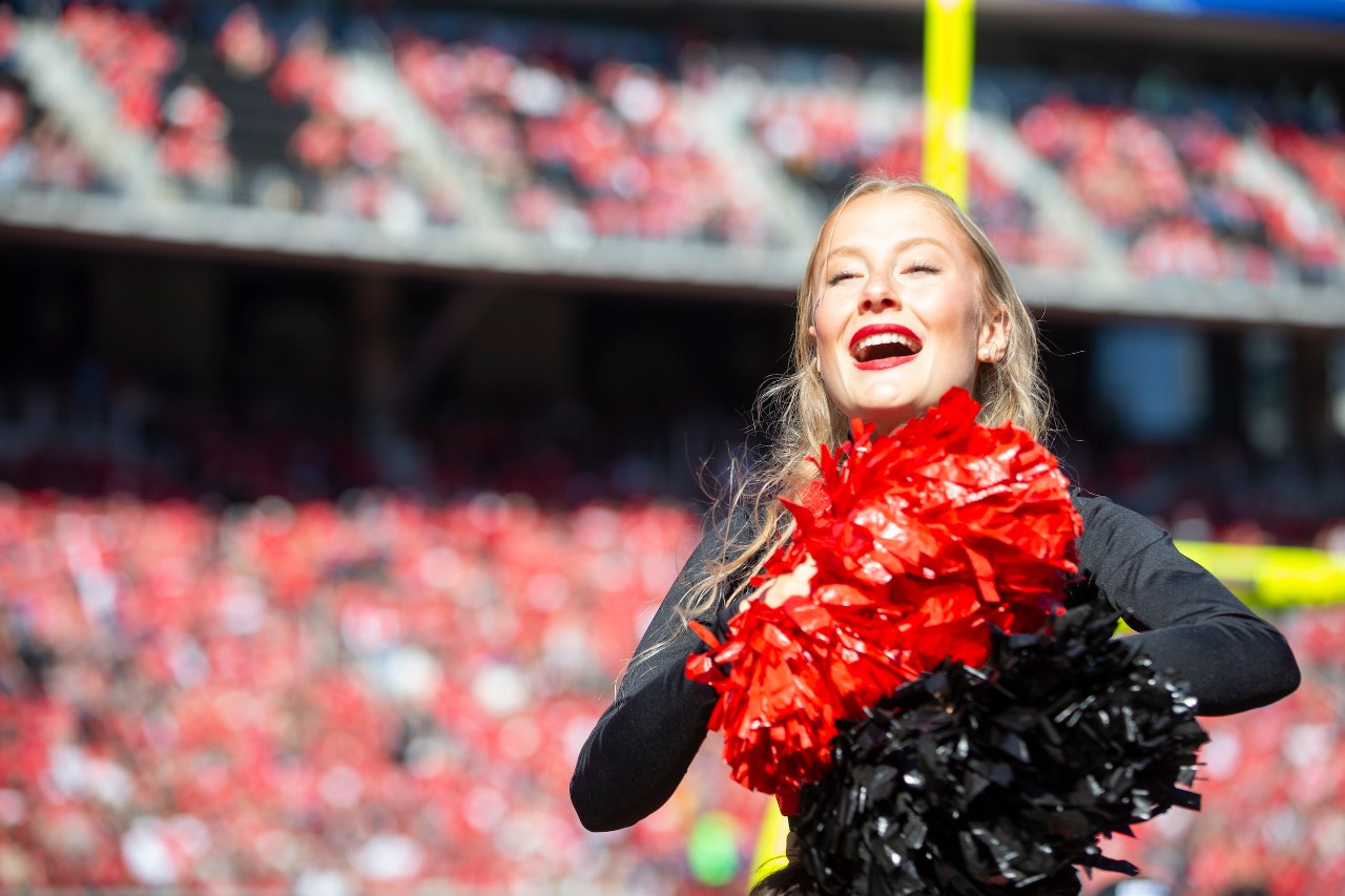 Cheerleader with red and black pompoms with packed stadium in background