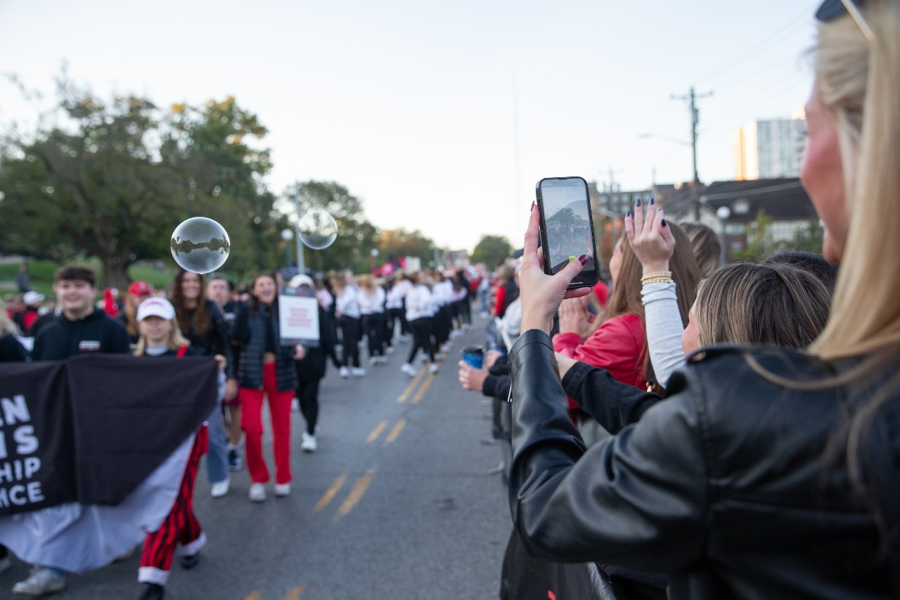many spectator watch and take cell phone photos of participants in the homecoming parade