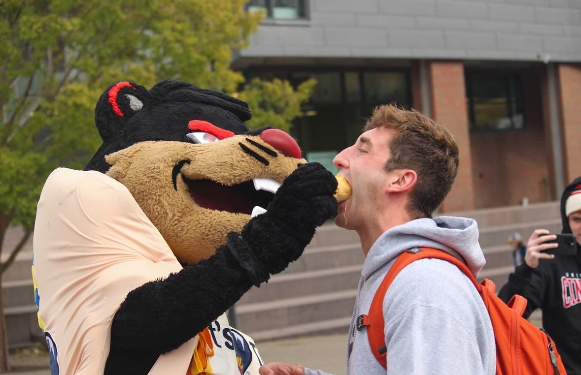 Bearcat Mascot feeds a hotdog to a student