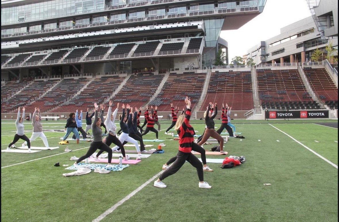 a dozen women participant in a yoga class on the field of Nippert Stadium