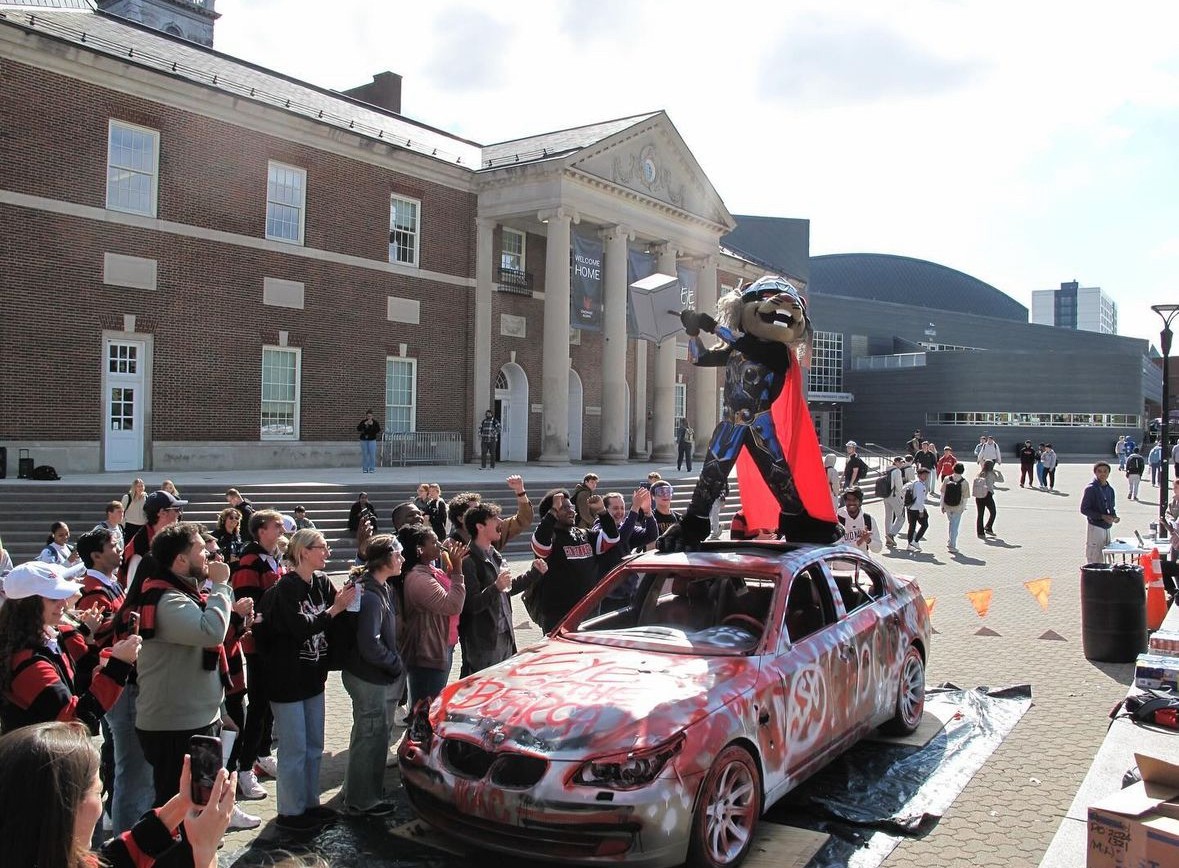 lots of student standing around a car being smashed by a hammer