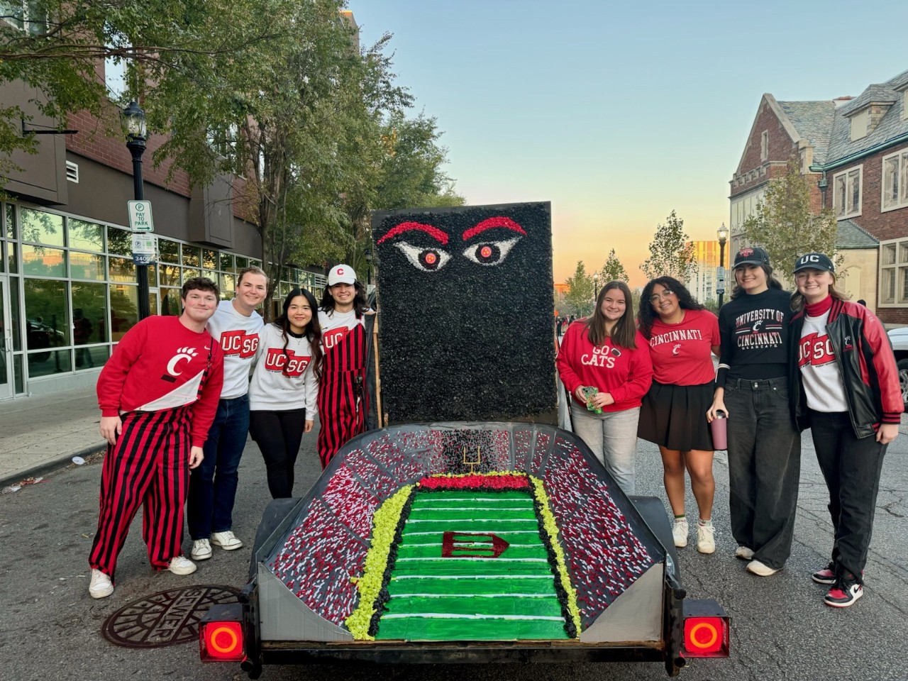 Eight UC students stand next to a parade float