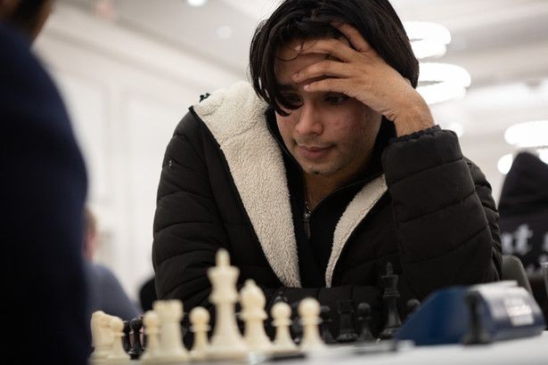 Aryan Balyan sits at a chess board with his hand cradling his head in concentration.