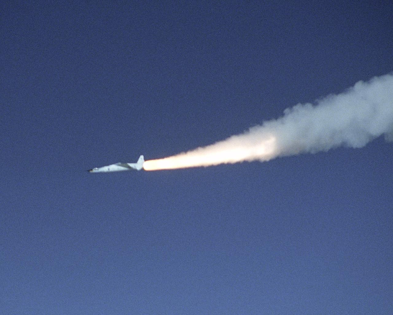A jet airplane leaves a trail of fire and smoke in an azure sky.