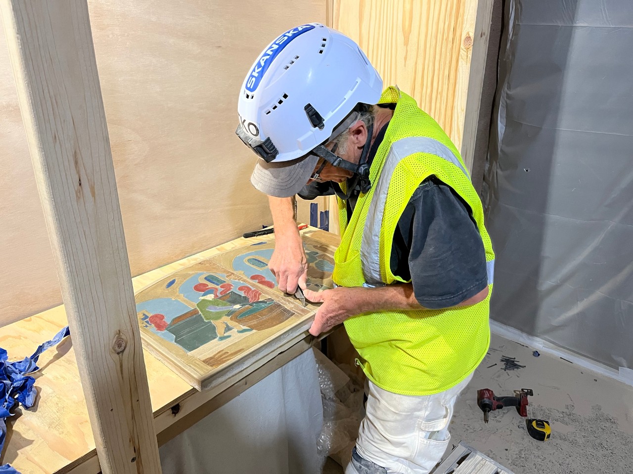 Tony Kalti in a hardhat and safety vest works on a piece of Rookwood tile.