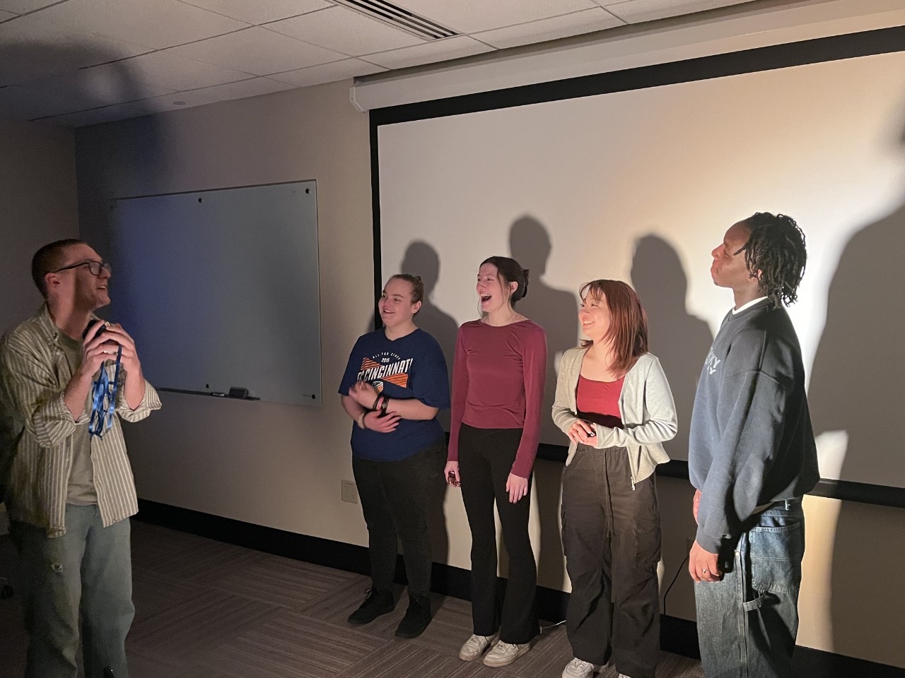 Students stand in a spotlight in front of a projector screen.