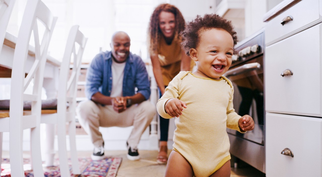 1439704792 Happy, baby and walking development of a toddler with parents feeling happy, proud and family love. Happiness, laughing and excited first walk of a kid showing growth with mama and father at home